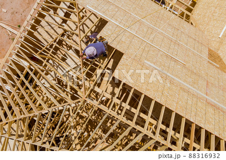 Aerial view of carpenter with plywood nailing on roof of in unfinished house Aerial view of carpenter with plywood nailing on roof of in unfinished house 88316932