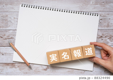 「実名報道」と書かれた積み木、ノート、ペン、手 88324490