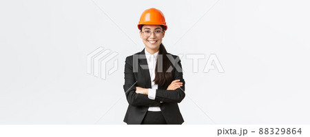 Professional smiling asian businesswoman in safety helmet and suit cross arms and looking confident, selling new buildings. Construction manager, engineer showing around, greeting investors 88329864