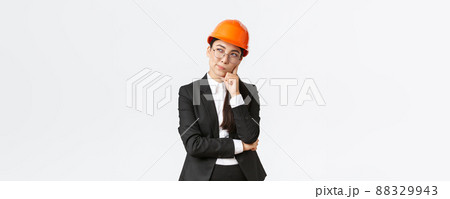 Thoughtful creative female asian chief architect, construction engineer thinking, wearing safety helmet and suit, pondering best choice for building, standing white background Thoughtful creative female asian chief architect, construction engineer thinking, wearing safety helmet and suit, pondering best choice for building, standing white background 88329943