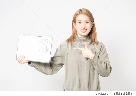 白い背景の前に立って小さいスケッチブックを見せている若い女性 88333185
