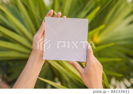 Women's hands in a tropical background holding a signboard paper, mockup Women's hands in a tropical background holding a signboard paper, mockup 88333631