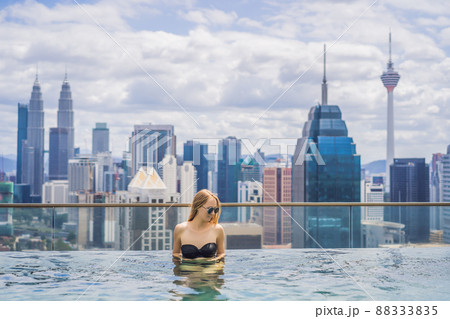 Young woman in outdoor swimming pool with city view in blue sky 88333835