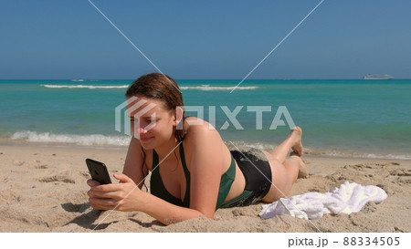 Pretty woman relaxes on the beach while texting with her cellphone Pretty woman relaxes on the beach while texting with her cellphone 88334505