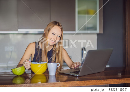 Beautiful woman having coffee and fruits for breakfast and looks into the laptop 88334897