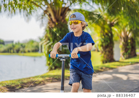 Child on kick scooter in park. Kids learn to skate roller board. Little boy skating on sunny summer day. Outdoor activity for children on safe residential street. Active sport for preschool kid 88336407