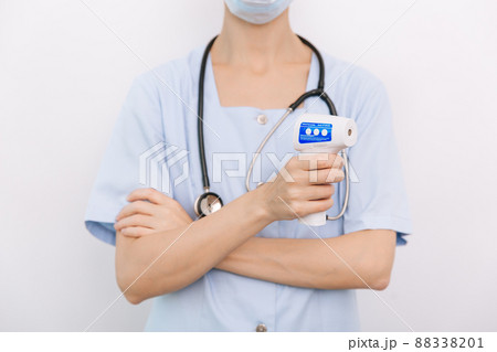 Temperature measurement gun in doctor hands. Close-up shot of doctor wearing protective surgical mask ready to use infrared isometric thermometer gun to check body temperature for virus symptoms. 88338201