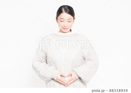 白い背景の前に立ってお腹に手を当てている女性 88338939