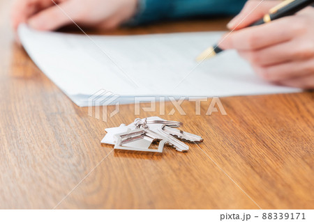 Close up of key with keychain lies on the table. Defocused hands signing a contract at the background. Concept of purchase of real estate and mortgage 88339171