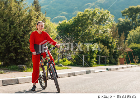 Sports lifestyle and Cycling. A young beautiful smiling woman in sportswear rides a Bicycle. In the background, the road and mountains, a Sunny day. Copy space 88339835