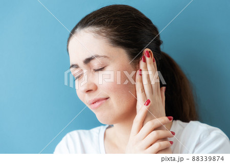 Portrait of a disgruntled young Caucasian woman covering her ear from pain or a loud sound. Blue background. The concept of deafness and ear diseases 88339874
