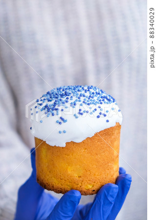 Hands in blue gloves hold Easter cake with white topping and blue sprinkles. Woman holding traditional Russian Easter cake. Homemade pie for spring holiday celebration Hands in blue gloves hold Easter cake with white topping and blue sprinkles. Woman holding traditional Russian Easter cake. Homemade pie for spring holiday celebration 88340029