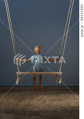 Portrait of boy on swing on the beach on dark sky background. Mystical back view portrait. Concept of childrens loneliness. 88341895