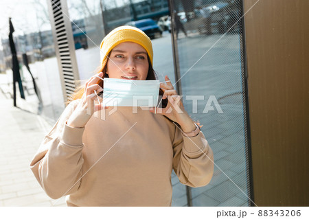 Happy smiling Woman taking off mask outdoor. Coronavirus ended. We are safe. Cheerful young woman in yellow hat removing protective mask off her face. Happy smiling Woman taking off mask outdoor. Coronavirus ended. We are safe. Cheerful young woman in yellow hat removing protective mask off her face. 88343206