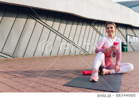 Fitness girl sitting with a bottle of water on the mat. 88344060