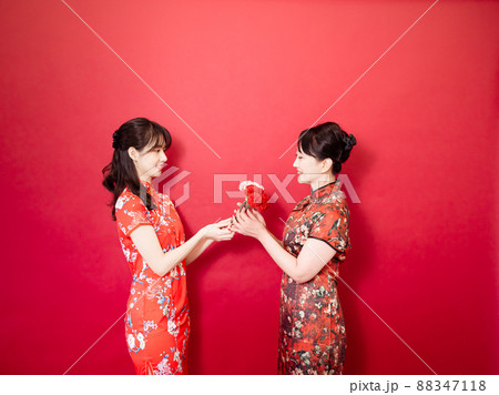 Portrait of asian young daughter and mother wearing traditional cheongsam qipao and smiling with flowers carnation in hands isolated on red background. 88347118