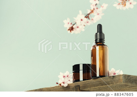 Amber glass dropper bottle with black lid, cream jar and spring flowers on glass shelf, green background. Skincare products , natural cosmetic. Beauty concept for face and body care, low angle view Amber glass dropper bottle with black lid, cream jar and spring flowers on glass shelf, green background. Skincare products , natural cosmetic. Beauty concept for face and body care, low angle view 88347605