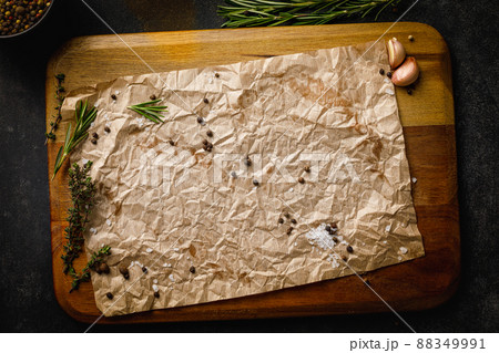 Wooden cutting board with sea salt, pepper and herbs covered with craft paper. Top view on black stone table with copy space Wooden cutting board with sea salt, pepper and herbs covered with craft paper. Top view on black stone table with copy space 88349991