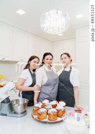 mother and daughters with Kraffins, easter cakes and Panettones in the kitchen. mother and daughters with Kraffins, easter cakes and Panettones in the kitchen. 88351125