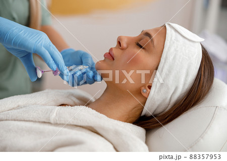 Side view of young woman getting hyaluronic acid injections in chin at beauty salon 88357953