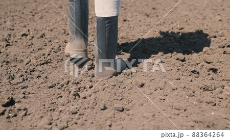 agriculture concept. plowed field land. farmer walks across field land rubber boots. work nature eco. farmland crop planting time. gardener works garden. legs boots close-up. farming concept. 88364264