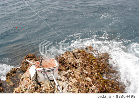 磯の先端 波洗う釣り座と準備されているウキふかせ釣り用の竿とコマセバッカンなど の写真素材