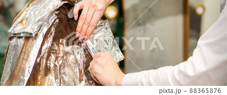 Hands of hairdresser dying hair applying foil for a brunette woman at the hairdressing salon, close up Hands of hairdresser dying hair applying foil for a brunette woman at the hairdressing salon, close up 88365876