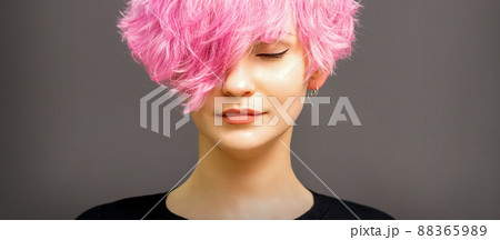 Beautiful young caucasian woman with short curly bob hairstyle dyed in pink color with closed eyes against dark gray background with copy space 88365989