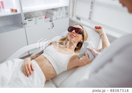 Joyful woman receiving laser epilation treatment in beauty salon Joyful woman receiving laser epilation treatment in beauty salon 88367318