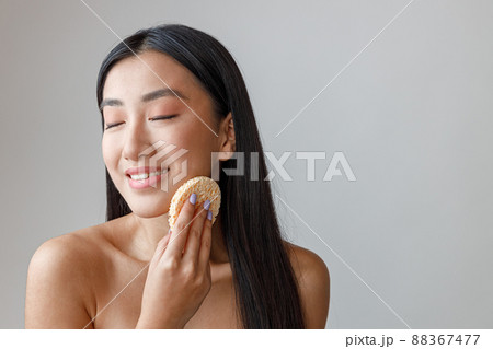 Joyful Asian woman cleaning face with cosmetic sponge Joyful Asian woman cleaning face with cosmetic sponge 88367477