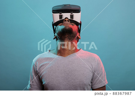 Male model looking up while he uses virtual reality glasses with interactive technology and 3d visual. Person using vr goggles with futuristic simulation to have fun experience in studio. Male model looking up while he uses virtual reality glasses with interactive technology and 3d visual. Person using vr goggles with futuristic simulation to have fun experience in studio. 88367987