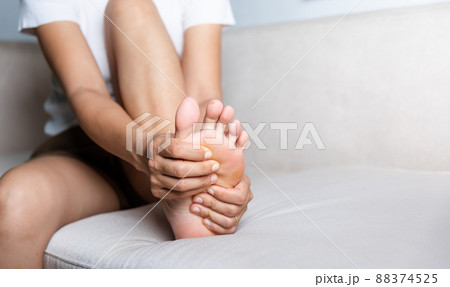 Asian woman sitting on sofa feeling pain in her foot at home 88374525