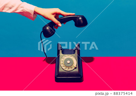 Retro objects, gadgets. Female hand holding handset of vintage phone isolated on blue and pink background. Vintage, retro fashion style. Pop art photography. Retro objects, gadgets. Female hand holding handset of vintage phone isolated on blue and pink background. Vintage, retro fashion style. Pop art photography. 88375414