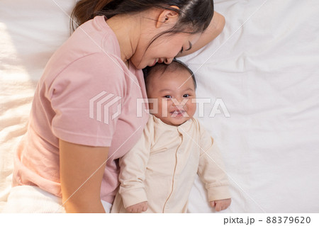Mom and kid are laying down and cuddling. Mom is kissing her son and both are smiling. Cute baby boy is look so happy and enjoy playing with mom. The baby has chubby and healthy. Mom and kid are laying down and cuddling. Mom is kissing her son and both are smiling. Cute baby boy is look so happy and enjoy playing with mom. The baby has chubby and healthy. 88379620