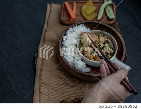 The hand is using chopsticks to pick up  Stir fried egg tofu with spring onion with Herbs vegetables served with steamed rice in wooden bowl. 88380962