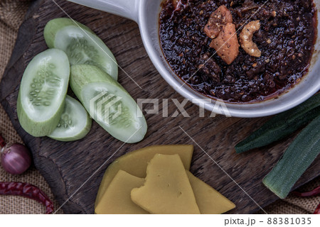 The hand is using pumpkin to scoop fried chili paste with shrimps (thai language nam prik pao) with the ingredient and fresh vegetables on wood background. 88381035