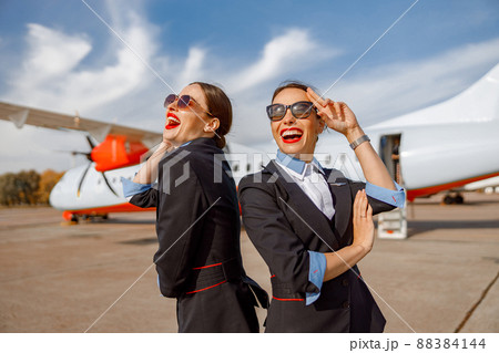 Two cheerful women stewardesses standing outdoors at airport Two cheerful women stewardesses standing outdoors at airport 88384144