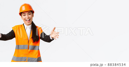 Friendly smiling asian female construction manager, engineer in safety helmet and reflective jacket, extending hands for greeting, welcome business partners, standing white background Friendly smiling asian female construction manager, engineer in safety helmet and reflective jacket, extending hands for greeting, welcome business partners, standing white background 88384534