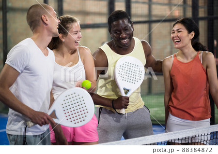 Four smiling men and women with padel rackets posing at court 88384872