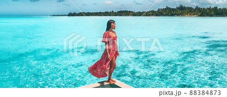 Travel vacation. Elegant asian woman relaxing at luxury pool resort overlooking turquoise ocean in red beach coverup maxi dress. Summer sun bikini lifestyle. Panoramic landscape banner 88384873