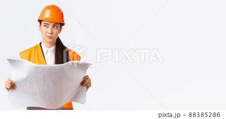 Thoughtful professional asian female construction manager, architect reading blueprints and looking away pondering, thinking, making decision while studying project plan, white background Thoughtful professional asian female construction manager, architect reading blueprints and looking away pondering, thinking, making decision while studying project plan, white background 88385286