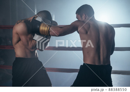 Two professional young muscular shirtless male boxers fighting in a boxing ring. Two professional young muscular shirtless male boxers fighting in a boxing ring. 88388550