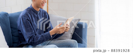 Young attractive asian man resting using browsing tablet computer on sofa at home. 88391928