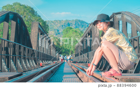 Asian woman is sitting on the River Kwai brigde, The memorial landmark of the World War 2 in Kanchanaburi, Thailand. Asian woman is sitting on the River Kwai brigde, The memorial landmark of the World War 2 in Kanchanaburi, Thailand. 88394600