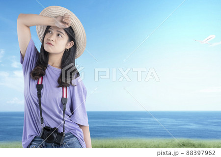Asian woman with hat and camera standing with unhappy expression 88397962