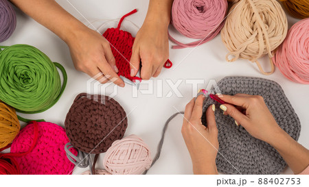 Top view of female hands with knitting on a white table. Two women are knitting baskets of cotton yarn. Top view of female hands with knitting on a white table. Two women are knitting baskets of cotton yarn. 88402753