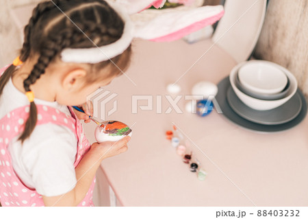 Child in bunny ears prepares colored eggs for Easter Child in bunny ears prepares colored eggs for Easter 88403232