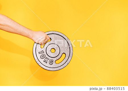 Hand holds ten-kilogram barbell dumbbell against yellow background Hand holds ten-kilogram barbell dumbbell against yellow background 88403515