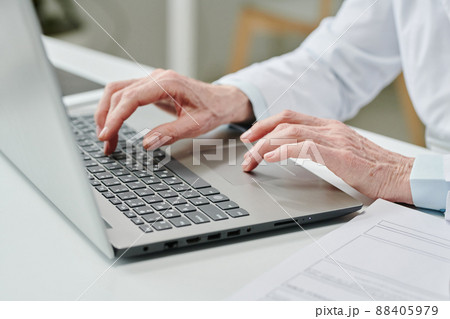 Hands of mature female clinician pressing buttons of laptop keyboard by desk Hands of mature female clinician pressing buttons of laptop keyboard by desk 88405979