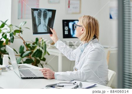 Mature blond female radiologist in whitecoat looking at x-ray image of lungs Mature blond female radiologist in whitecoat looking at x-ray image of lungs 88406014